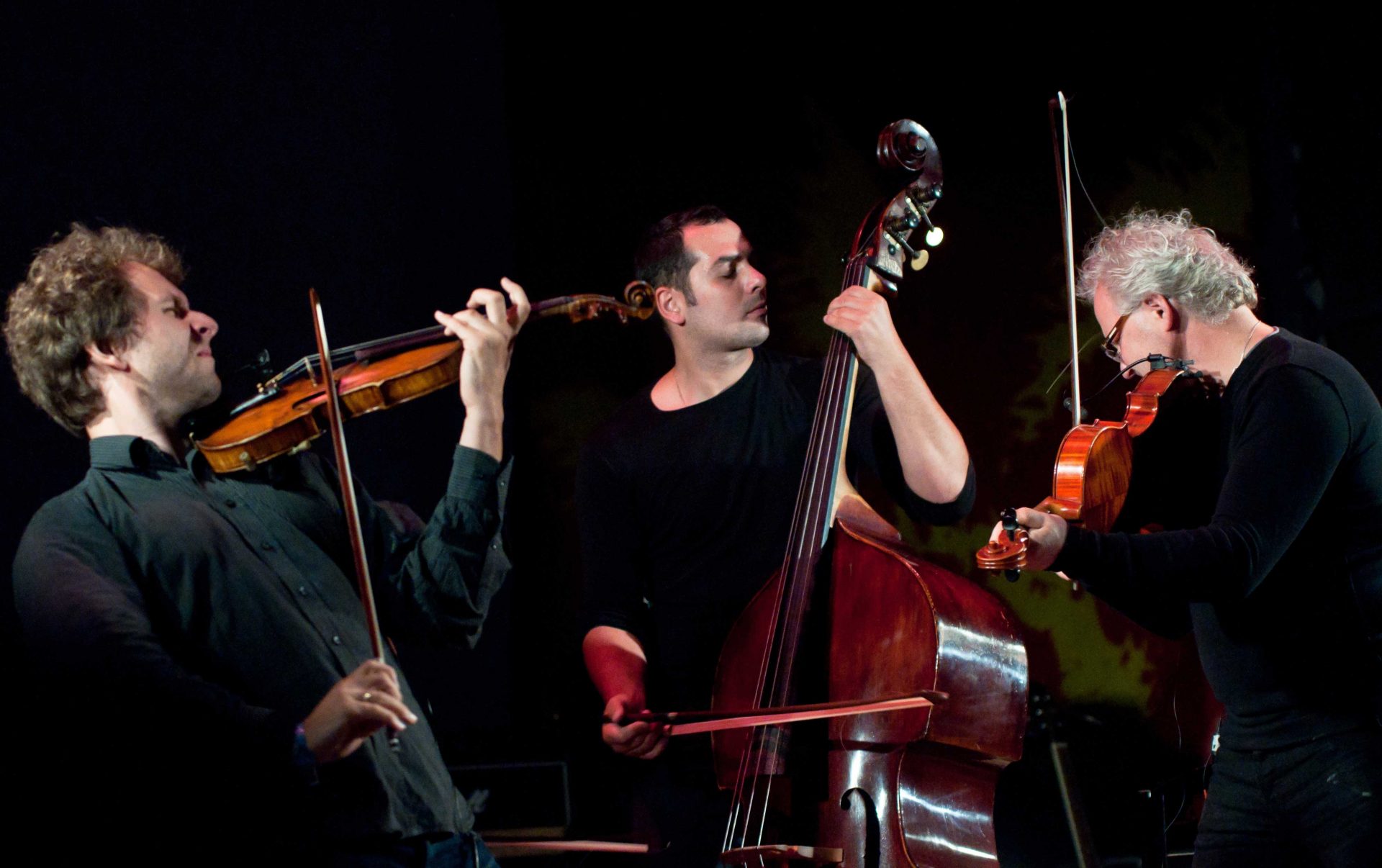 Двоє музикантів грають на скрипках, а третій музикант — на контрабасі смичком на нічній сцені фестивалю в Унежі